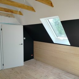 Remonty i wykończenia u szwagrów - Poddasze po remoncie: czarna ściana, drewniana boazeria, białe drzwi i okno dachowe, widoczne drewniane belki stropowe.
