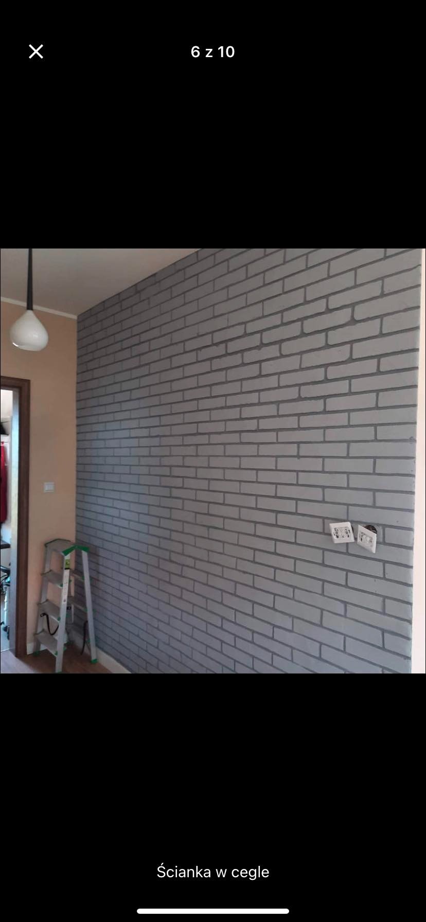 Ściana wewnętrzna pomalowana na szaro imitująca cegłę, z widocznymi gniazdkami elektrycznymi i drabiną w tle.