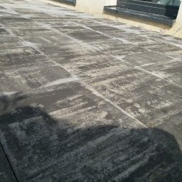 Dawid Barczyk - Ułożona kostka brukowa w odcieniach szarości tworząca taras przy budynku z ciemnymi ramami okiennymi.