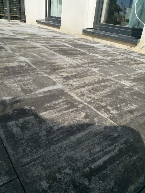 Ułożona kostka brukowa w odcieniach szarości tworząca taras przy budynku z ciemnymi ramami okiennymi.