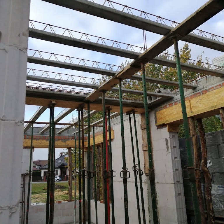 Budowa domu w Gnieźnie: widok na zbrojenie stropu i murowane ściany nośne z betonu komórkowego, wsparte stemple budowlane.