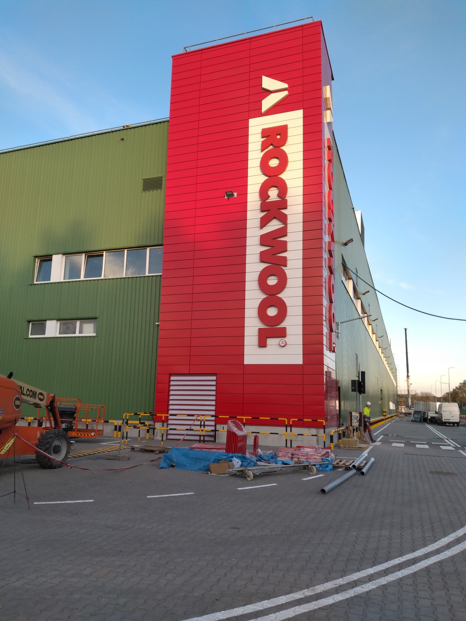 Montaż elewacji z wełny mineralnej Rockwool na budynku przemysłowym, widoczny podnośnik koszowy i pracownik w kasku.