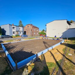 Budorem Developer sp. zo.o. - Zbrojenie fundamentów pod budowę domu jednorodzinnego. Widoczni pracownicy w niebieskich koszulkach. Ujęcie w słoneczny dzień, z perspektywy szerokokątnej.