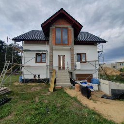 Budorem Developer sp. zo.o. - Niedokończony dom z białym styropianem na elewacji, ceglanym wykończeniem i rusztowaniami. Widoczne materiały budowlane i elementy konstrukcyjne.