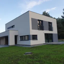 Nowoczesny, dwukondygnacyjny dom z płaskim dachem, wykończony w bieli i szarości, z garażem w bryle budynku, otoczony trawnikiem i drzewami.