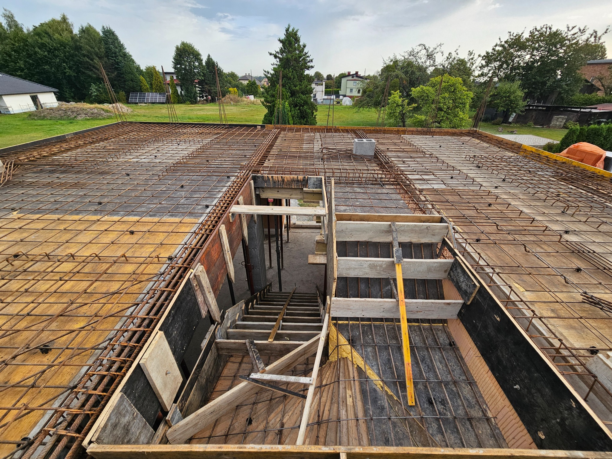 Zbrojenie stropu z deskowaniem i przygotowanym otworem na schody w domu jednorodzinnym. Widok z góry na plac budowy w słoneczny dzień.