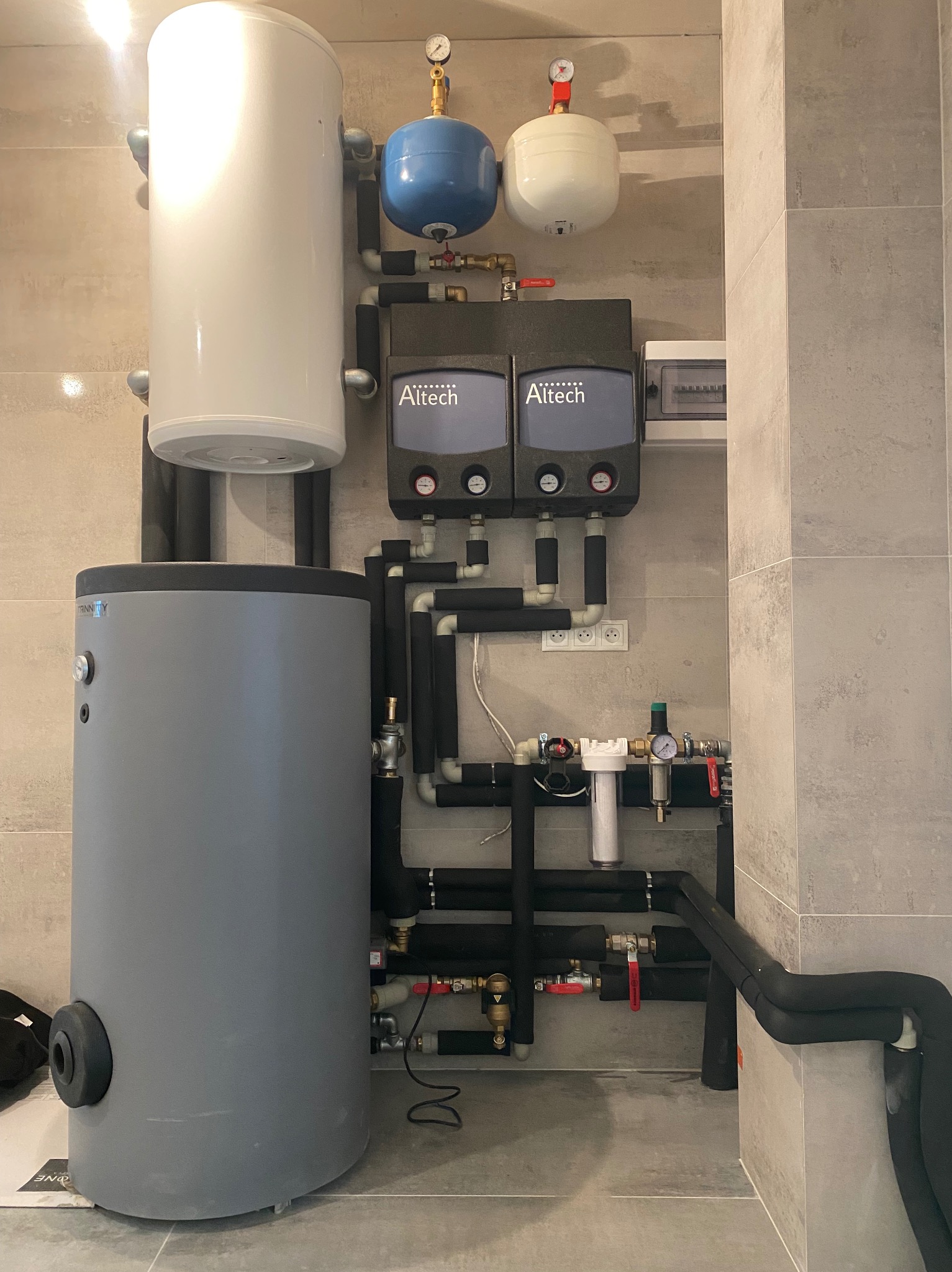Zestaw kotłowni z dwoma zbiornikami buforowymi, naczyniami przeponowymi i rozdzielaczami Altech, instalacja w pomieszczeniu wyłożonym płytkami imitującymi kamień.