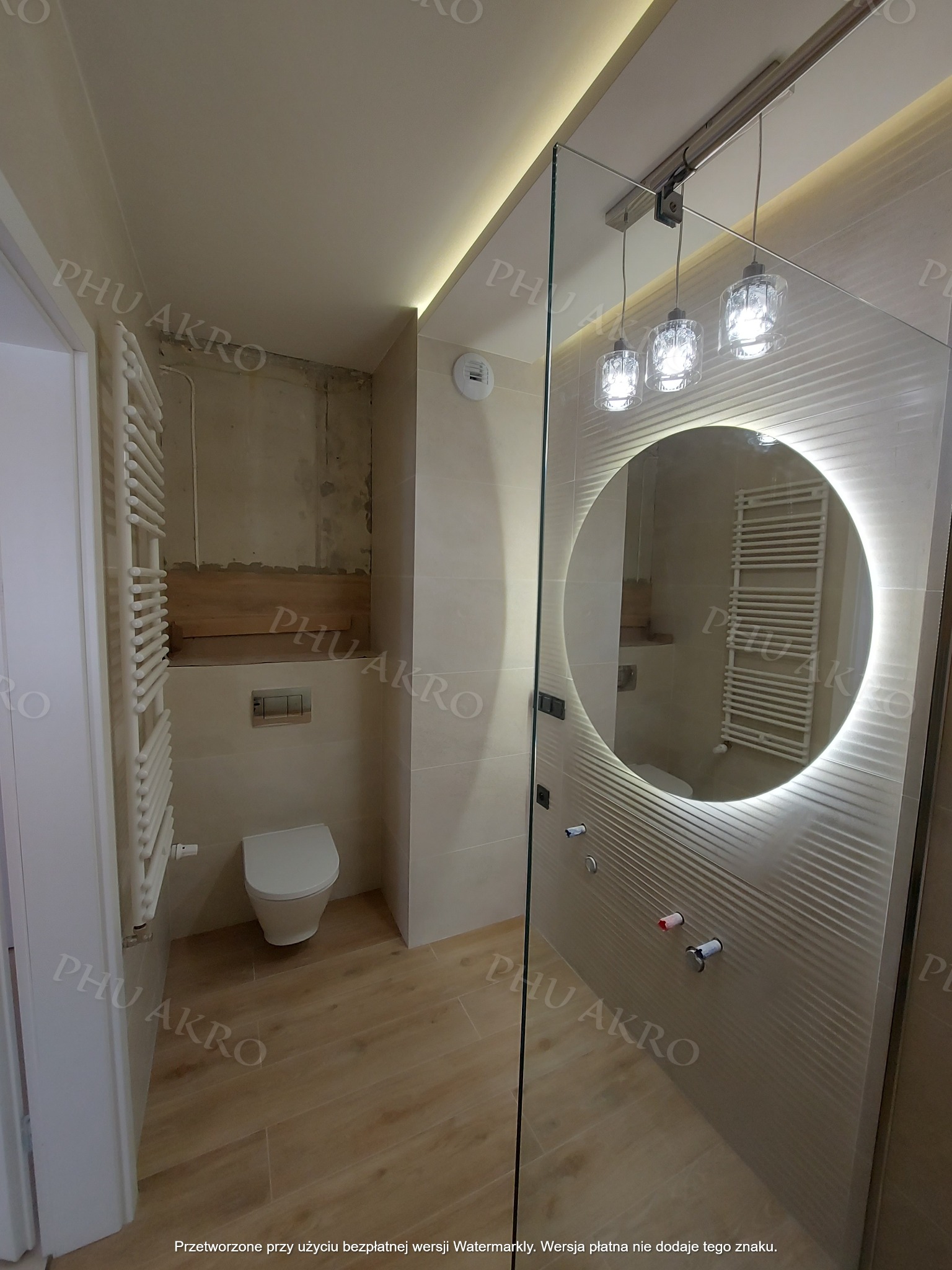 Nowoczesna łazienka w trakcie wykańczania: widoczne płytki strukturalne, okrągłe lustro z podświetleniem LED i częściowo wykończona ściana z instalacją.