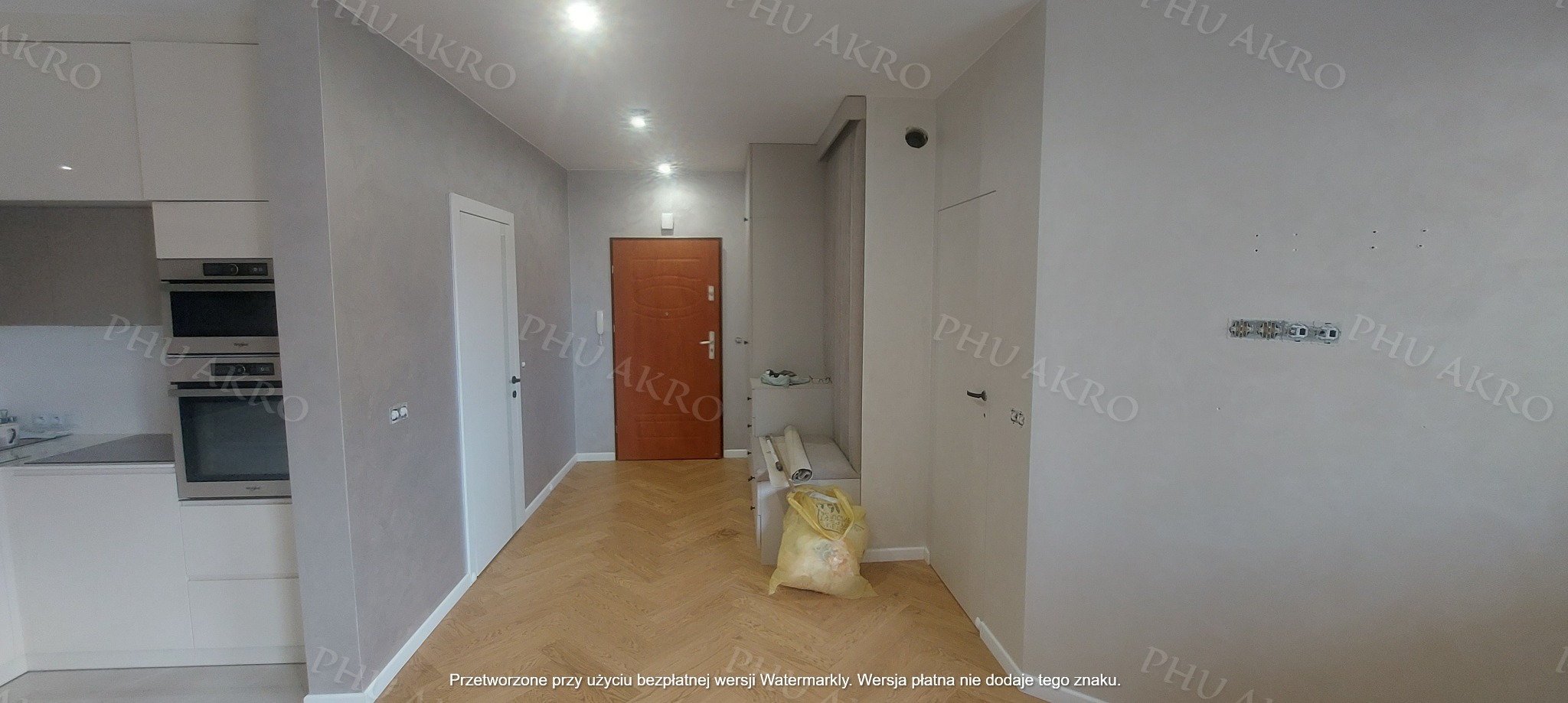 Jasne wnętrze po odświeżeniu: parkiet w jodełkę, gładkie ściany w odcieniach szarości, białe drzwi i zabudowa kuchenna. Widoczne puszki elektryczne.