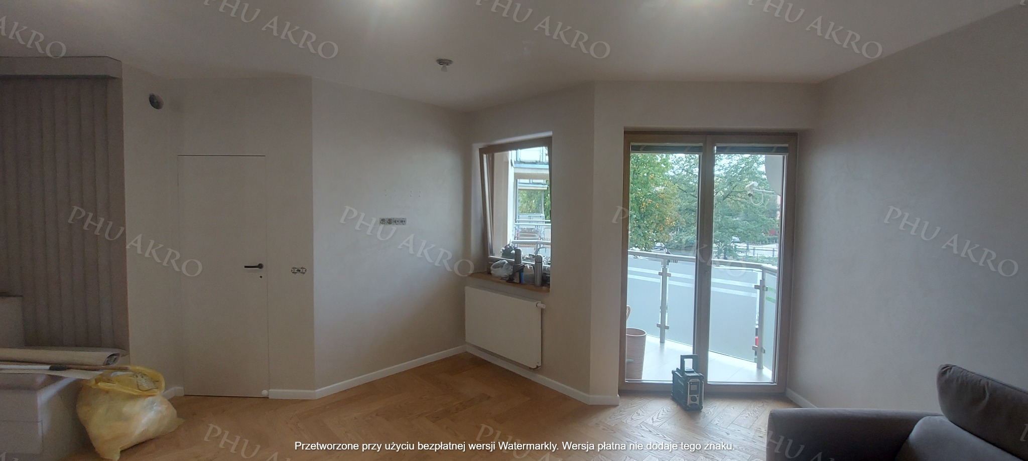 Jasne wnętrze po malowaniu ścian z parkietem w jodełkę. Widoczne okno balkonowe, grzejnik i drzwi. Na podłodze torba z odpadami budowlanymi.