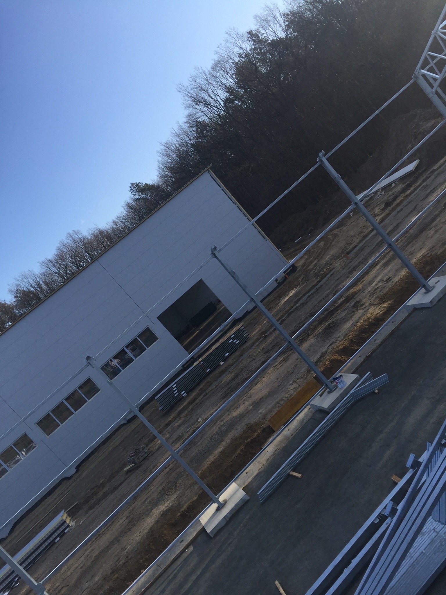 Wznoszenie hali stalowej: widok z góry na konstrukcję w trakcie budowy, widoczne metalowe słupy i elementy fasady, teren przygotowany pod dalsze prace.