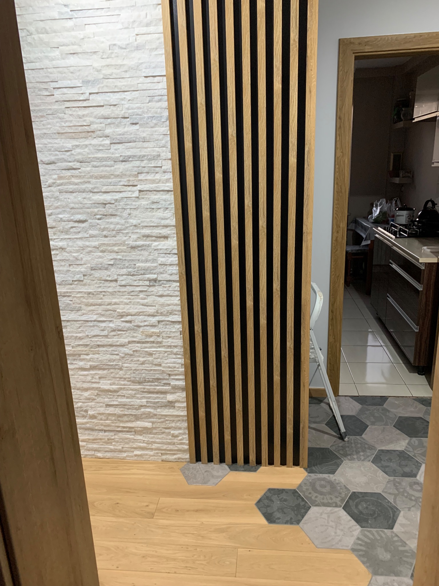 Wnętrze z dekoracyjną ścianą z białej cegły, panelem ściennym z drewnianych listew na czarnym tle oraz podłogą z drewnianych paneli przechodzącą w szare heksagonalne płytki.