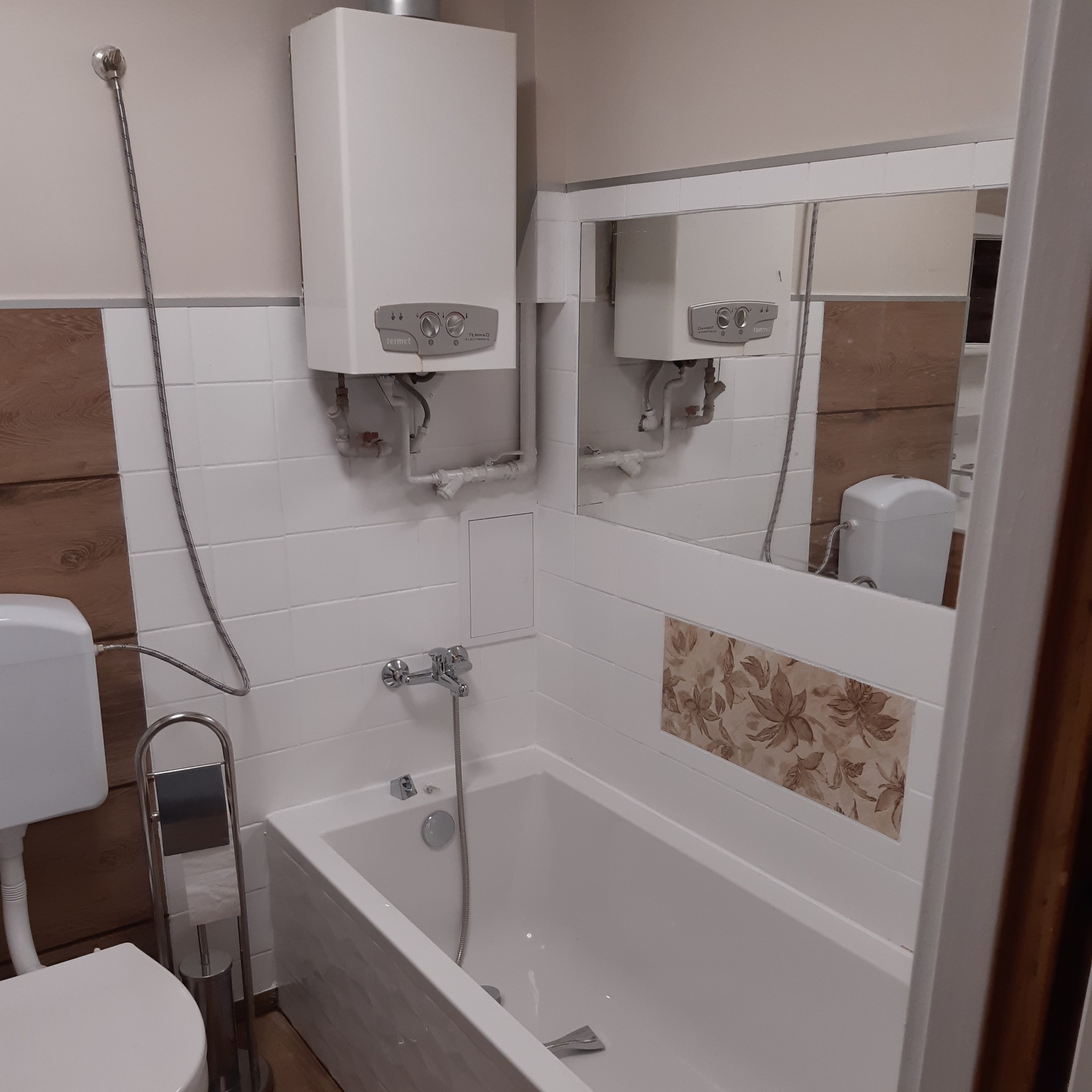 Biała łazienka po remoncie z wanną, umywalką i piecem gazowym Termet, widoczna w lustrze toaleta.