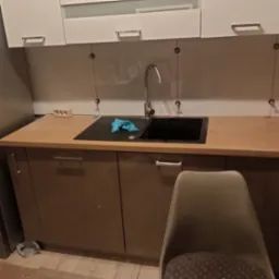 Kuchnia w trakcie remontu: zamontowany zlew i bateria, ale widoczne ślady po zdjętych płytkach na ścianie, z zachowanymi plastikowymi krzyżykami dystansowymi.