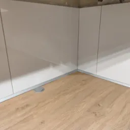 Jasne panele podłogowe z listwą przypodłogową i gładkimi, białymi szafkami w Kobiórze, widoczny okrągły otwór w podłodze.