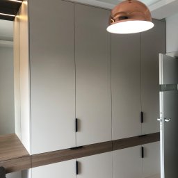 Ostap Vaskiv - Wbudowana szafa z szarymi frontami i drewnianymi akcentami, zintegrowana z biurkiem, oświetlona miedzianą lampą wiszącą i listwami LED.