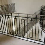 Metalowa balustrada schodowa z prostokątnymi i okrągłymi elementami dekoracyjnymi, widok z góry na białe schody.