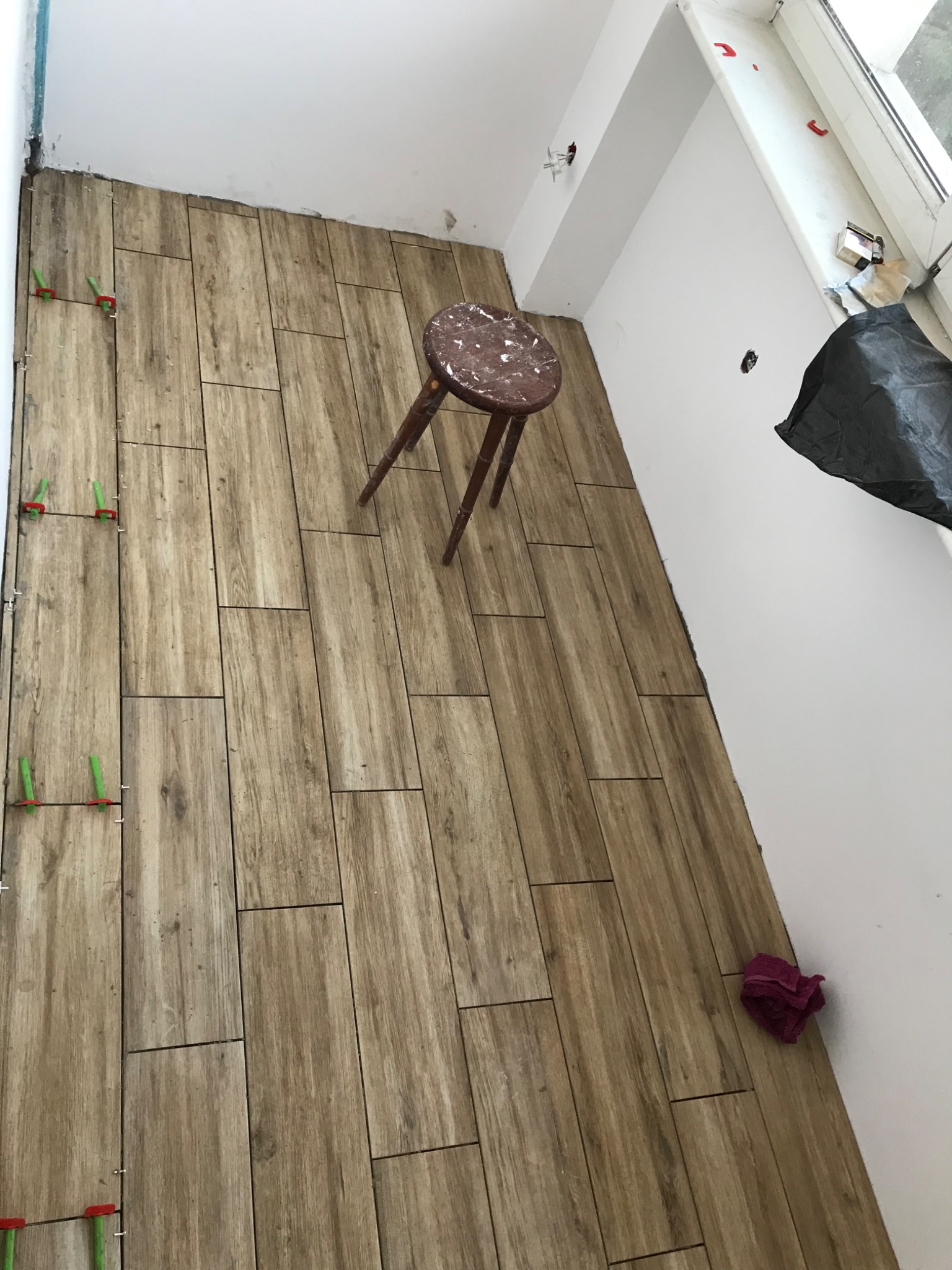 Układanie płytek drewnopodobnych na podłodze w łazience, widoczne krzyżyki dystansowe i stołek malarski.