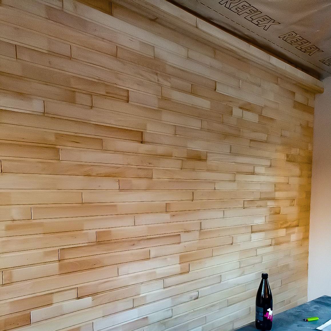 Ściana wykończona jasnym drewnem ułożonym w poziome pasy, widoczna butelka i zielony długopis na blacie.