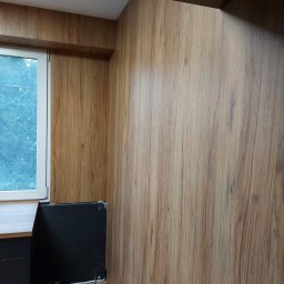 ONYKS Aneta Bytniewska - Wykończona ściana w okleinie drewnopodobnej, z widocznym fragmentem okna i blatu. Ujęcie z niskiego kąta, podkreślające fakturę i kolorystykę materiału.