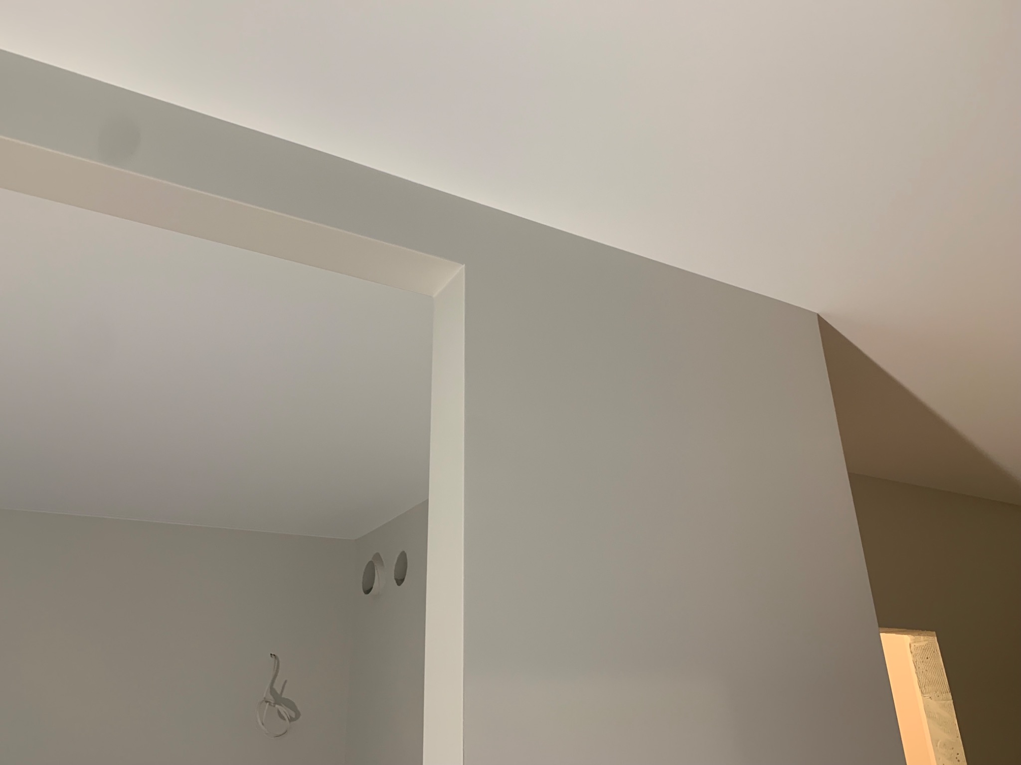 Świeżo pomalowane, jasnoszare wnętrze z widocznymi otworami wentylacyjnymi i wystającymi przewodami elektrycznymi, ukazujące detale wykończenia ścian i sufitu w trakcie remontu.