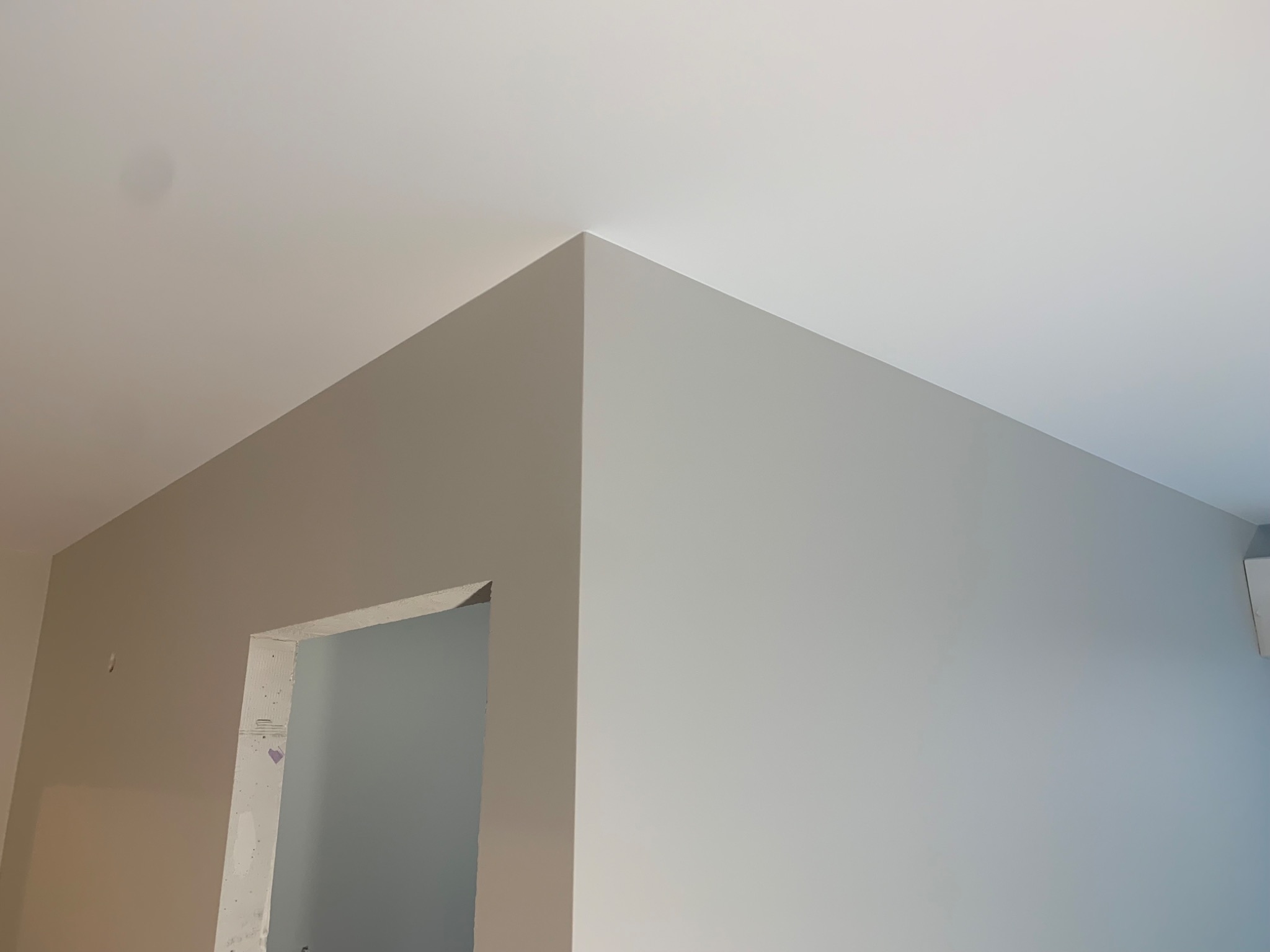 Pomieszczenie po remoncie, ściany pomalowane na szaro, sufit biały, widoczny fragment ościeżnicy drzwiowej w stanie surowym.