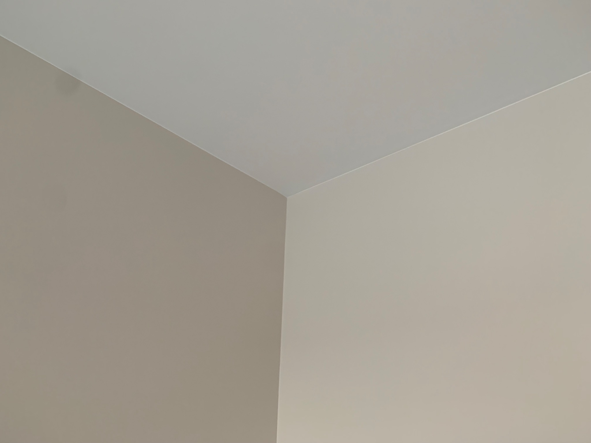 Fragment rogu pokoju po malowaniu, gdzie ściany w odcieniach beżu spotykają się z białym sufitem, tworząc czyste i minimalistyczne połączenie.