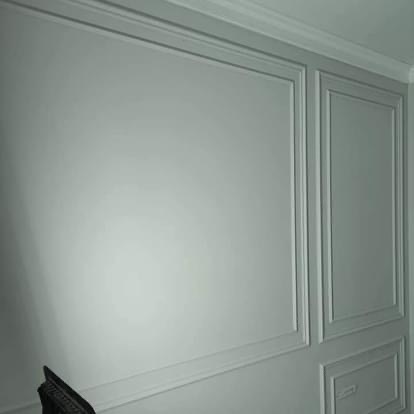 Ściana z dekoracyjnymi panelami w kolorze szaro-zielonym, wykończona listwami przysufitowymi, oświetlona z lewej strony.