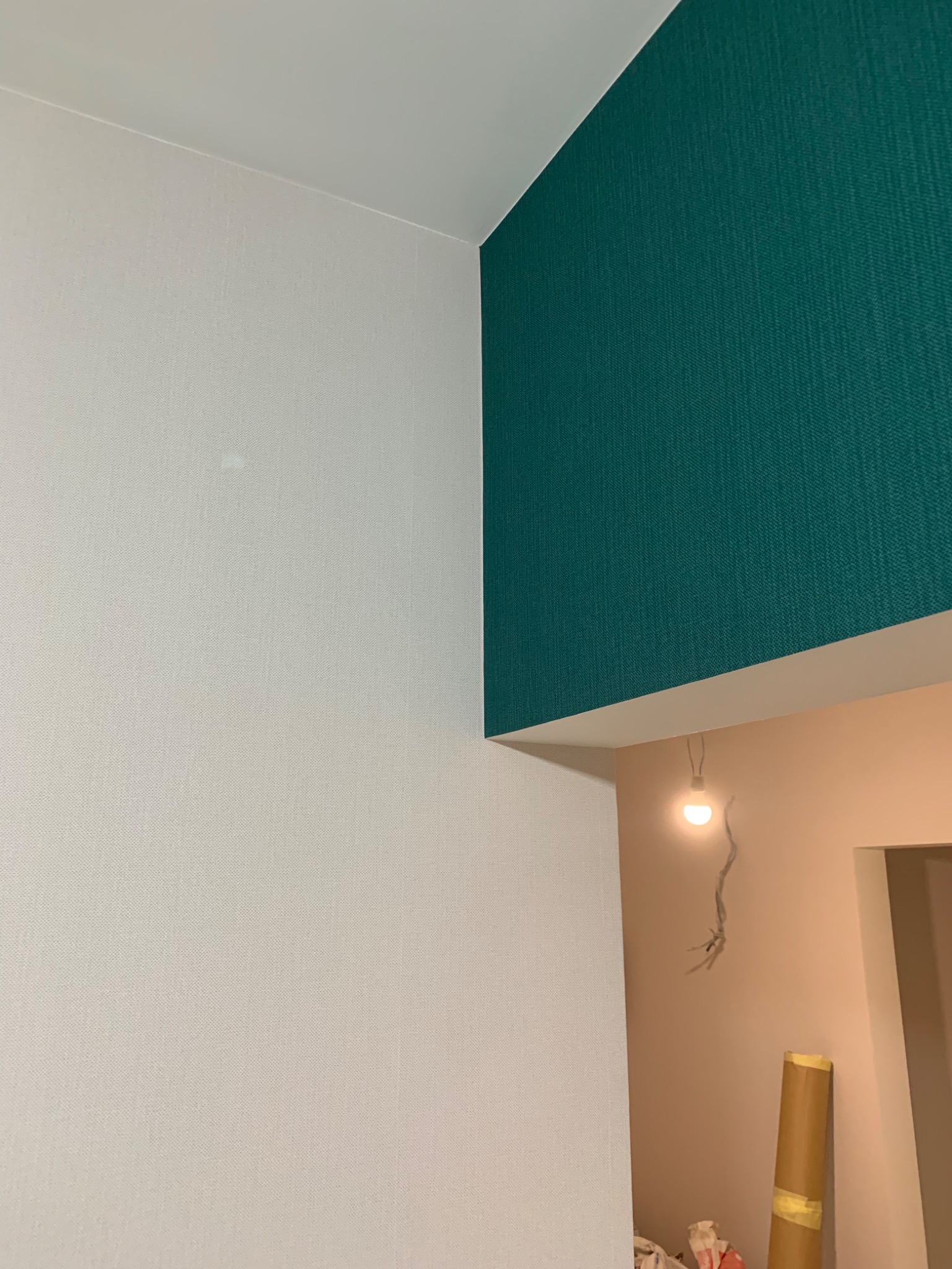 Fragment wykończonego wnętrza we Wrocławiu z białą teksturowaną ścianą, kontrastującą z ciemnozieloną ścianą w rogu, widoczne niedokończone oświetlenie i materiały budowlane.