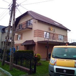 Adam Dombke gamma - Dwupiętrowy dom z balkonami, ocieplony z zewnątrz, z widocznym samochodem dostawczym firmy remontowej na pierwszym planie i anteną satelitarną na elewacji.