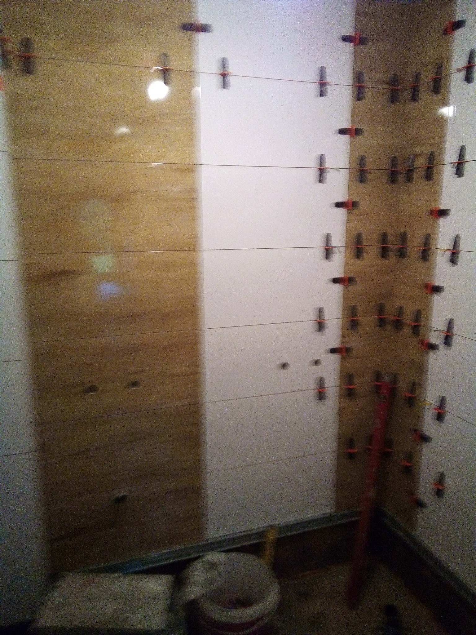 Ściana w trakcie układania płytek imitujących drewno, z użyciem poziomicy i systemu poziomowania płytek, widoczne otwory na kołki.