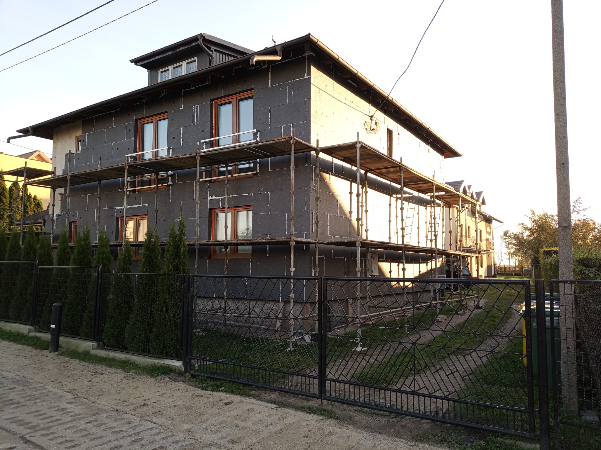 Dom jednorodzinny w trakcie ocieplania elewacji zewnętrznej, widoczne rusztowania i płyty izolacyjne EPS w kolorze grafitowym.