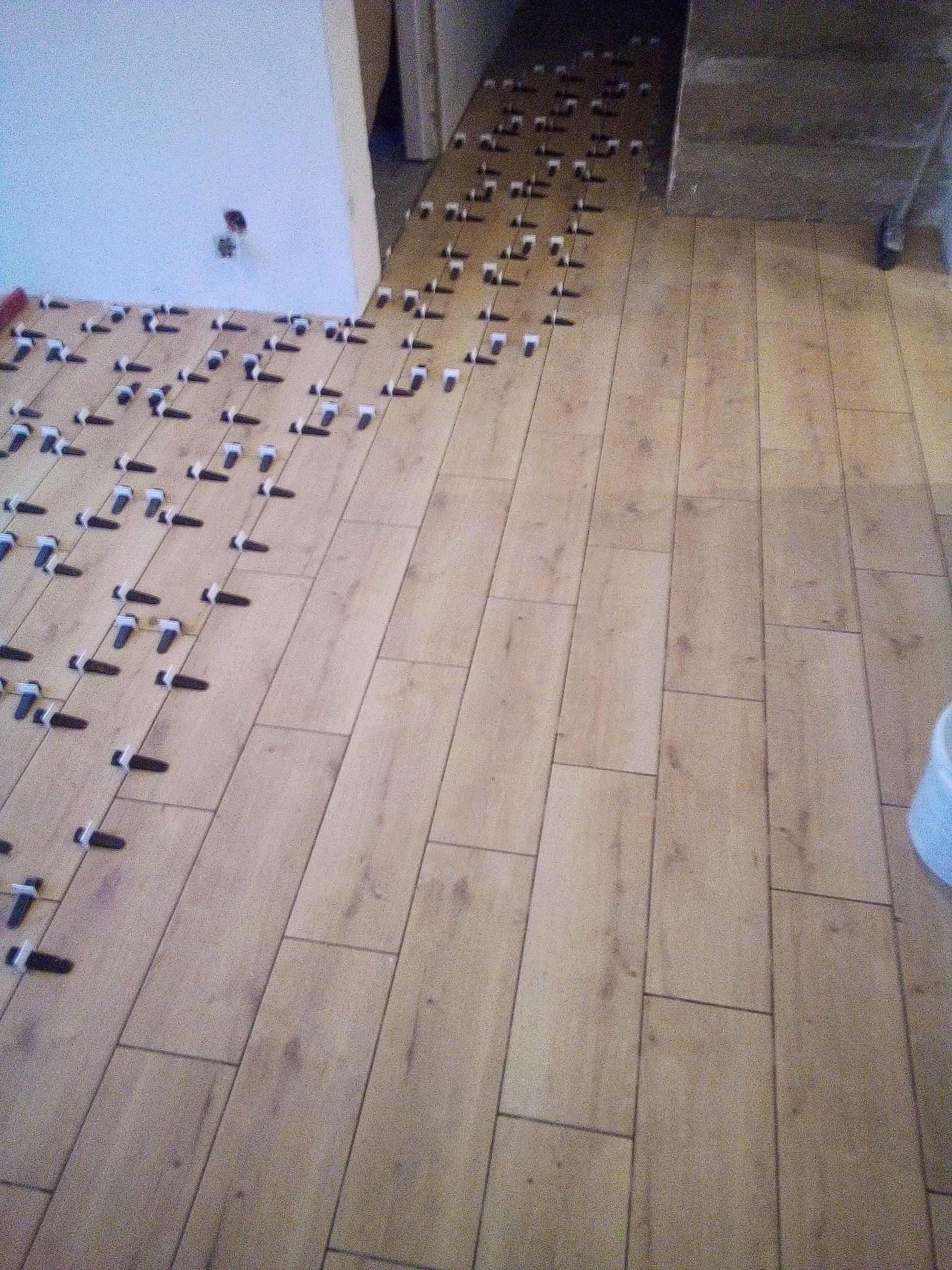 Układanie paneli podłogowych z wykorzystaniem klipsów poziomujących, widoczne fragmenty ściany i drzwi.