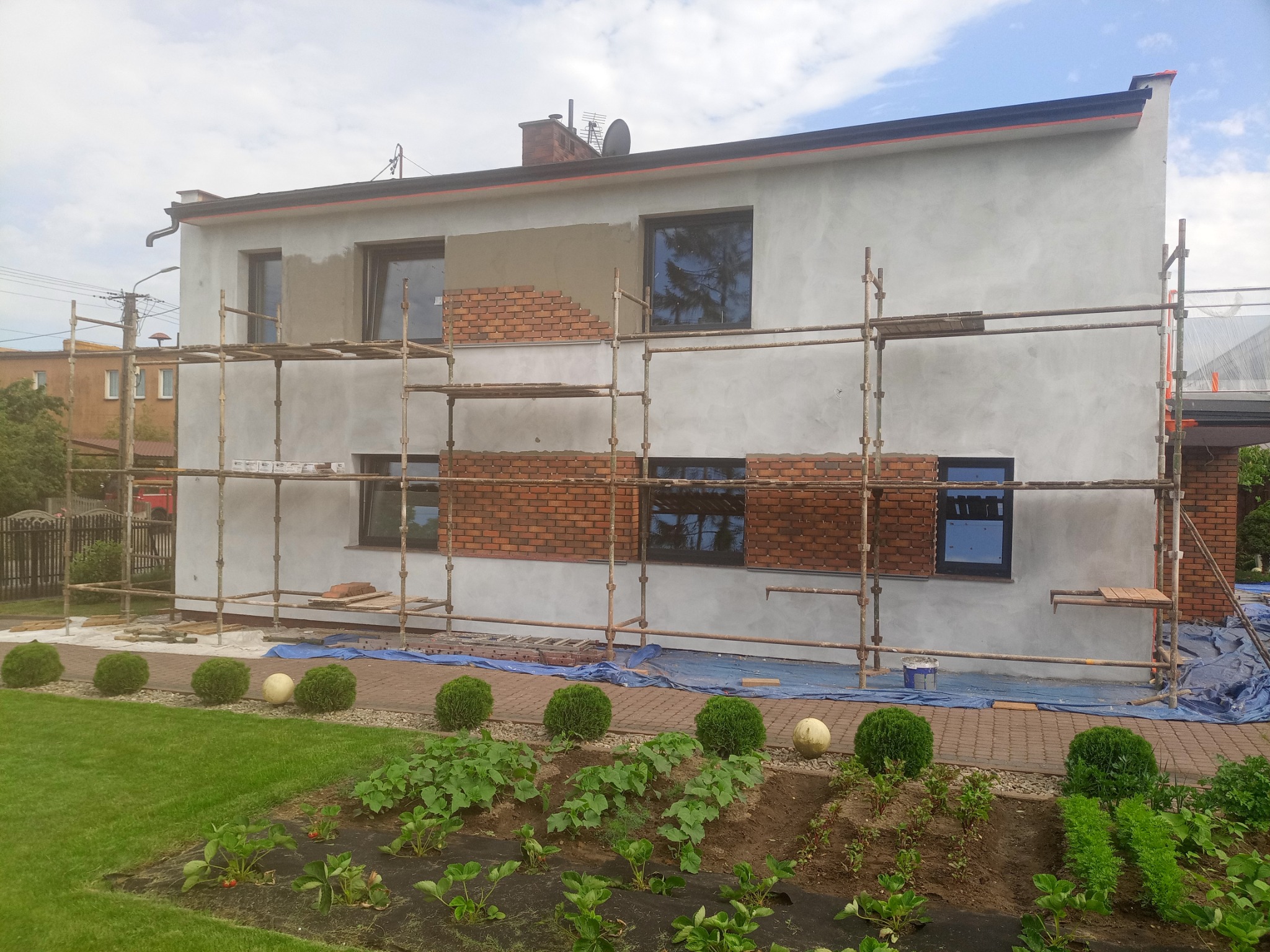 Dom jednorodzinny w trakcie układania cegły elewacyjnej, widoczne rusztowania i przygotowane podłoże, Władysławowo.