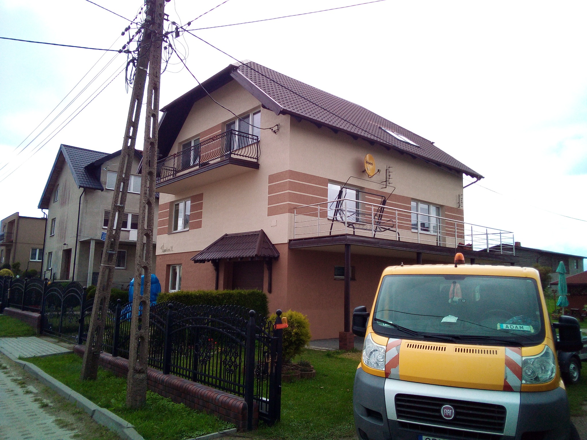 Dwupiętrowy dom z balkonami, ocieplony z zewnątrz, z widocznym samochodem dostawczym firmy remontowej na pierwszym planie i anteną satelitarną na elewacji.