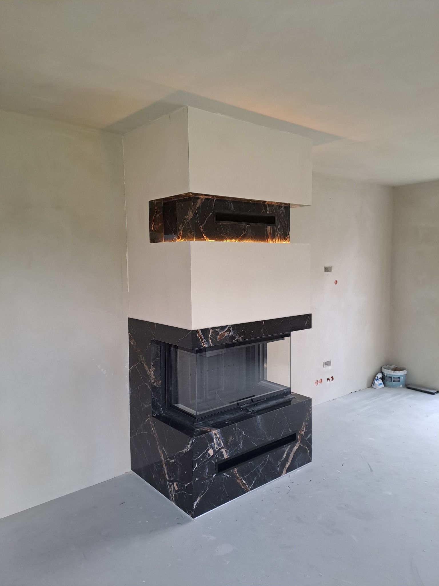 Nowoczesna obudowa kominkowa z czarnego marmuru z białymi elementami w Skomielnej Białej, w trakcie wykończenia wnętrza.