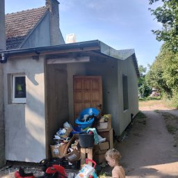 Docieplenia elewacje - Surowy budynek w trakcie prac wykończeniowych elewacji, z oknami bez szyb, zabałaganiony teren budowy z zabawkami dziecięcymi. Nowa elewacja w jasnym kolorze kontrastuje z ciemnym dachem i zielenią...