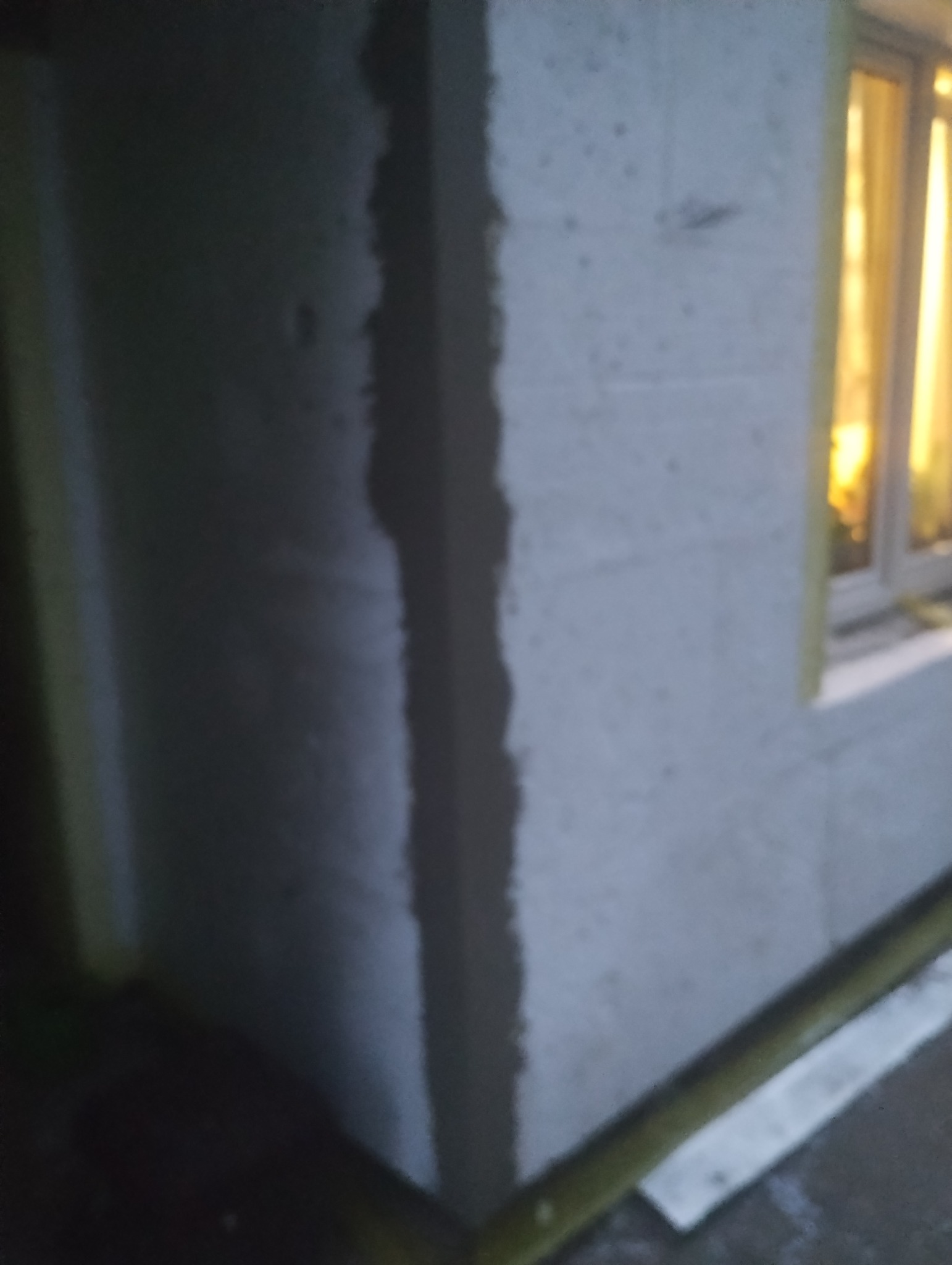 Fragment ściany budynku z widoczną świeżo nałożoną warstwą zaprawy wyrównującej, przygotowaną pod dalsze prace, z oknem w tle.