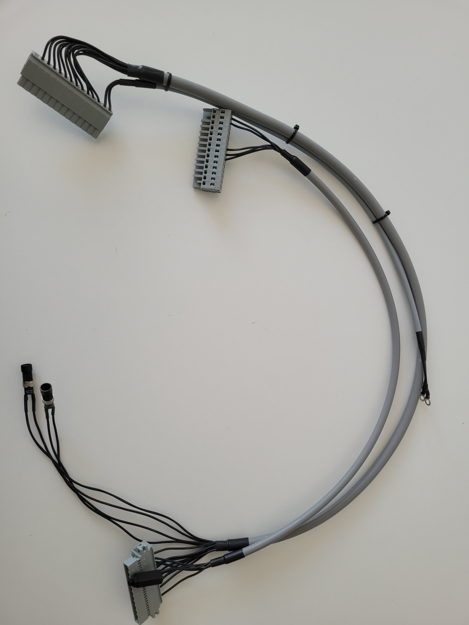 Kabel telekomunikacyjny z szarymi przewodami i złączami, zabezpieczony czarnymi opaskami zaciskowymi i termokurczliwą izolacją, ułożony na białym tle.