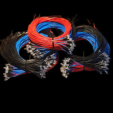 Zestaw zwiniętych kabli światłowodowych w kolorach czarnym, niebieskim i czerwonym, z widocznymi złączami, na ciemnym tle.