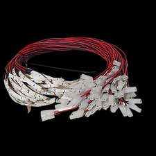 Zestaw przewodów z białymi złączkami i taśmą LED, ułożony na czarnym tle, widoczne czerwone i czarne przewody.