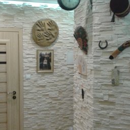 Usługi Remontowo-Budowlane RENOMA - Wykończona ściana z dekoracyjną okładziną imitującą kamień, ozdobiona zegarem, wachlarzami i pamiątkami, oświetlona listwą LED pod sufitem, z widocznym fragmentem drewnianych drzwi.