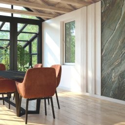 MM-Studio Projektowanie Wnętrz Marcin Martela - Jasna jadalnia z dużym oknem i marmurową ścianą. Pomarańczowe krzesła otaczają czarny stół na parkiecie. Widoczny fragment ogrodu za oknem i logo projektanta wnętrz.