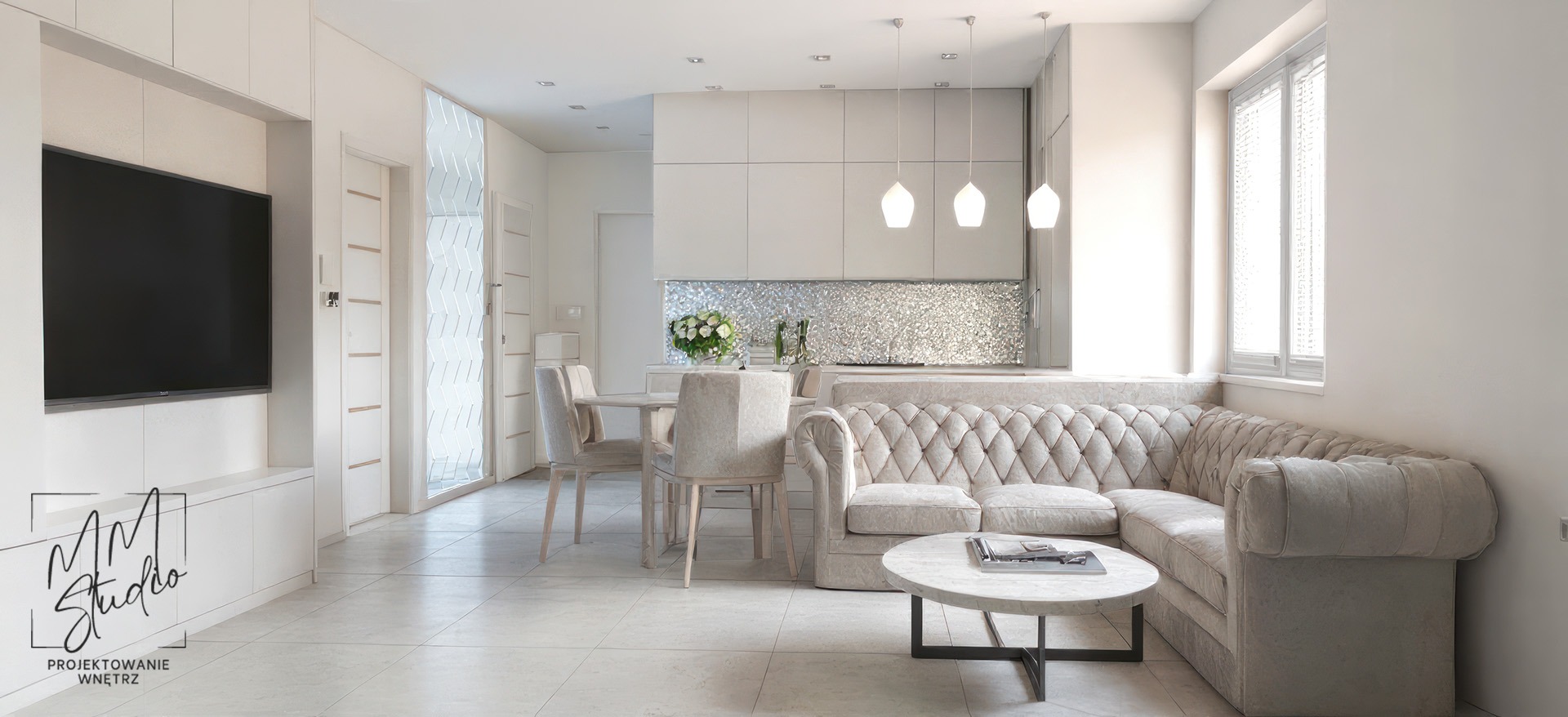 Jasne, przestronne wnętrze z narożną sofą Chesterfield, marmurowym stolikiem i błyszczącą mozaiką na ścianie. Widoczny fragment aneksu kuchennego i telewizor.