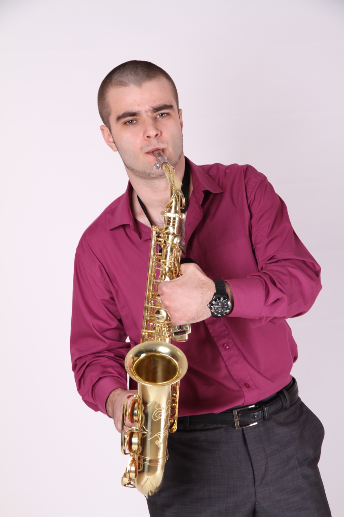 Młody saksofonista w purpurowej koszuli gra na złotym saksofonie na białym tle.