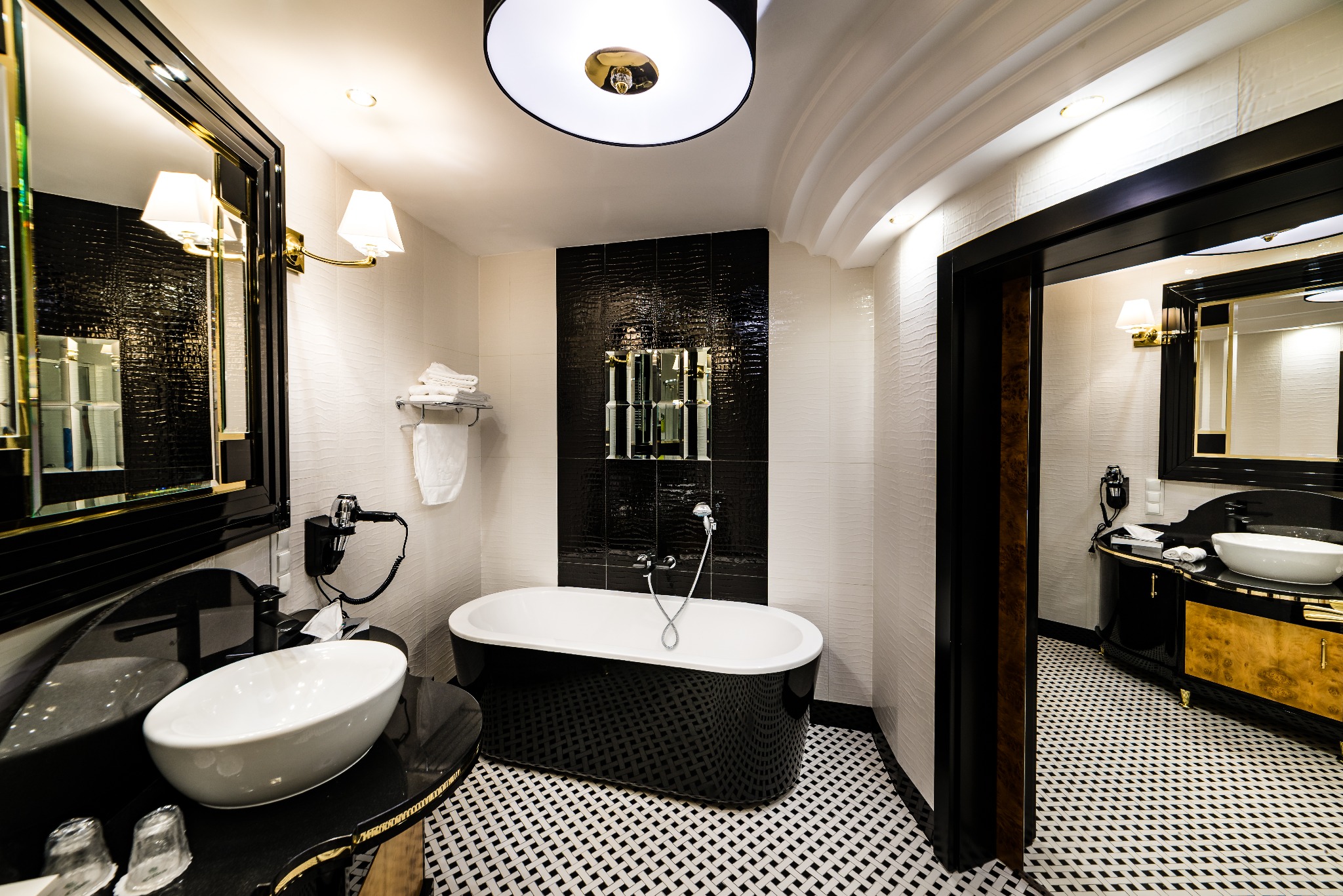 Nowoczesna łazienka w czarno-białej kolorystyce z wolnostojącą wanną, umywalką na blacie i lustrami w ozdobnych ramach.