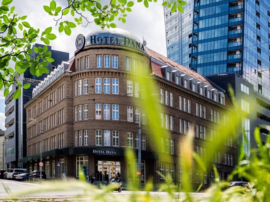 Elewacja hotelu Dana z kopułą, widok z poziomu ulicy przez zieloną trawę, na tle nowoczesny wieżowiec.