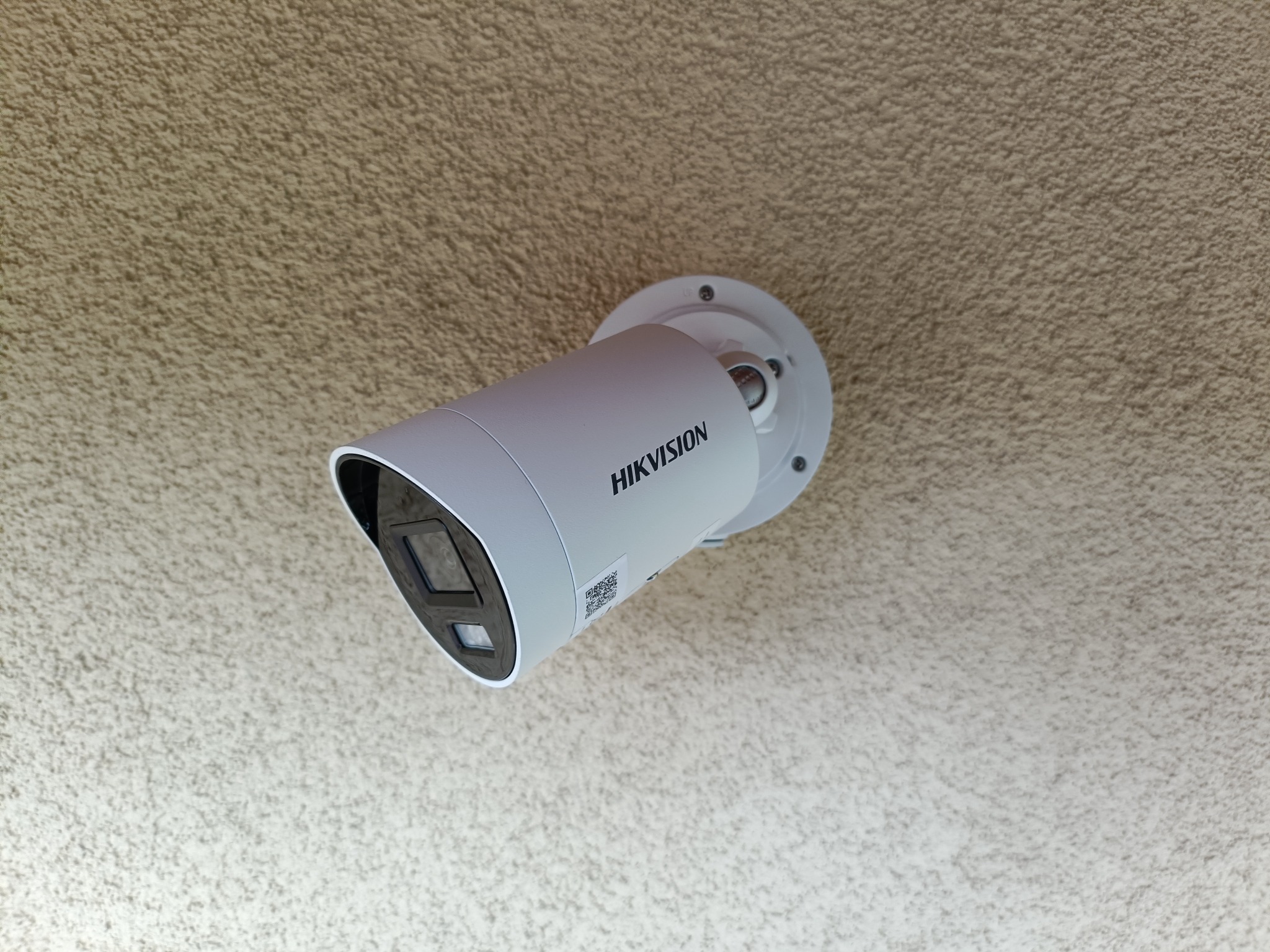 Kamera monitoringu Hikvision zamontowana na teksturowanym suficie. Widoczny korpus kamery, uchwyt montażowy i fragment sufitu. Kąt ujęcia od dołu.