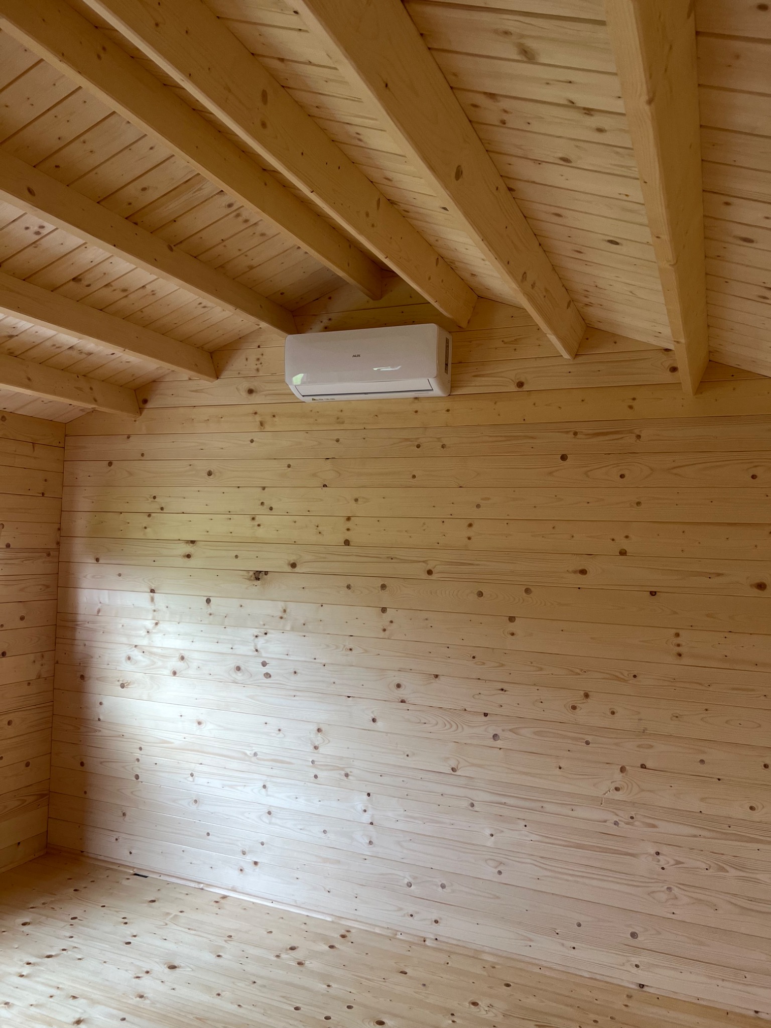 Wnętrze pomieszczenia wykończonego boazerią z jasnego drewna z zamontowanym na ścianie klimatyzatorem.