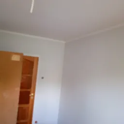 Świeżo pomalowane na szaro ściany w pokoju, widoczny fragment drewnianych drzwi oraz wiadro z farbą i kuweta malarska.